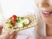 Woman eating crispbread with soft cheese, cress and tomato