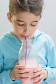 Little girl drinking strawberry milk out of bottle with straw