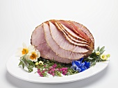 Roast ham, partly carved, on platter with edible flowers