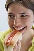 Young woman biting into hot dog with ketchup
