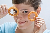 Young woman holding up two deep-fried onion rings