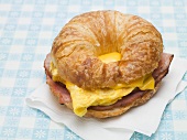 Croissant with scrambled egg, cheese & bacon on paper napkin