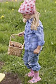 Little girl holding basket full of bark mulch in garden