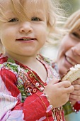 Kleines Mädchen hält Reiswaffel, Frau im Hintergrund