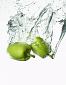 Zwei grüne Paprika fallen ins Wasser