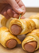 Hand pushing cocktail stick into sausage roll