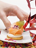Hand reaching for cracker topped with smoked salmon