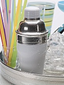 A cocktail shaker, ice cubes, glasses and straws