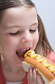Mädchen in Hot Dog mit Senf beissend