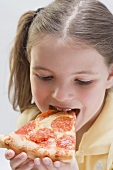Mädchen beisst in ein Stück Salamipizza
