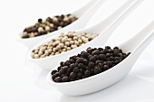 Different types of peppercorns in three spoons (close-up)