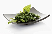 Clusters of green peppercorns with leaves in dish