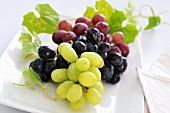 Green and red grapes with leaves on plate