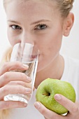 Woman holding apple and drinking glass of water