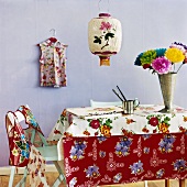 Tisch mit farbenfroher Tischdecke, bunten Blumen in der Vase und Malutensilien