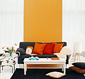 Schwarze Couch mit roten und orangen Zierkissen vor sonnengelber Wand