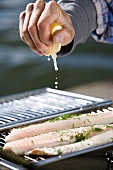 Mann beträufelt Fisch mit Zitronensaft (Schweden)