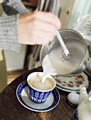 Making cappuccino: pouring frothed milk into cup