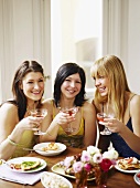 Drei junge Frauen mit Drinks beim Esstisch