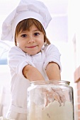 Little girl taking flour out of jar with both hands