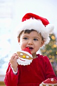 Kleines Mädchen mit Nikolausmütze isst einen Keks