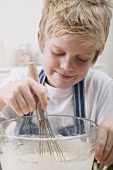 Boy stirring baking mixture in glass bowl with whisk