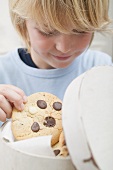 Boy taking chocolate chip cookie out of biscuit tin