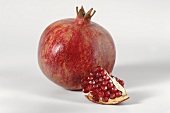 A piece of pomegranate in front of a whole pomegranate