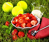 Fresh strawberries, cream and tennis balls in grass