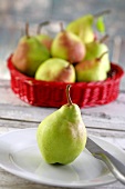 A pear on a plate in front of a basket of pears