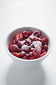 Raspberries and strawberries with icing sugar in white bowl