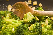 Stirring broccoli in a frying pan with a wooden spoon
