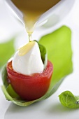 Pouring olive oil on tomato stuffed with mozzarella and basil