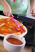 Small child spreading tomato sauce on pizza dough