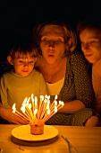 Mother and daughters blowing out candles on birthday cake