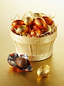 Foil-wrapped chocolate eggs in and beside a woodchip basket