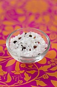 A small glass dish of sea salt with spices and peppercorns