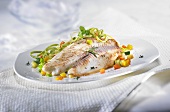 Cooked tilapia fillets on spring vegetables and ribbon pasta