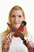 Female chef holding crossed kitchen knife and wooden spoon