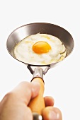 Hand holding fried egg in a small frying pan