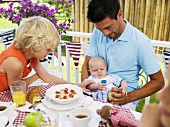 Familie mit Baby frühstückt im Freien