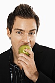 Junger Mann beisst in einen grünen Apfel