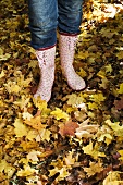 Frau steht mit Gummistiefeln auf Herbstlaub