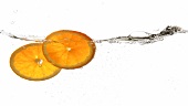 Zwei Orangenscheiben fallen ins Wasser