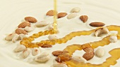 Pouring honey onto almonds & cashew nuts on white couverture