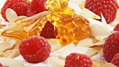 Pouring honey over cream with raspberries & flaked almonds