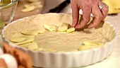 Making apple tart: laying apple slices in lined tart tin