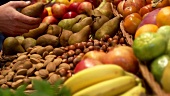 Fruit and nuts on a market stall, hand taking a pear