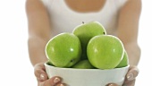 Junge Frau hält eine Schale mit grünen Äpfeln