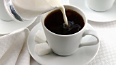 Kaffee und Milch in eine Tasse gießen